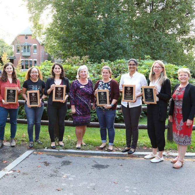 		Nine people stand in a line; six of them hold plaques
	