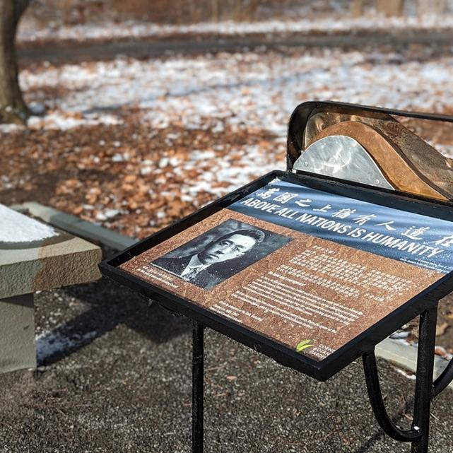 		In a natural areas, a stone bench is next to an interpretive sign
	