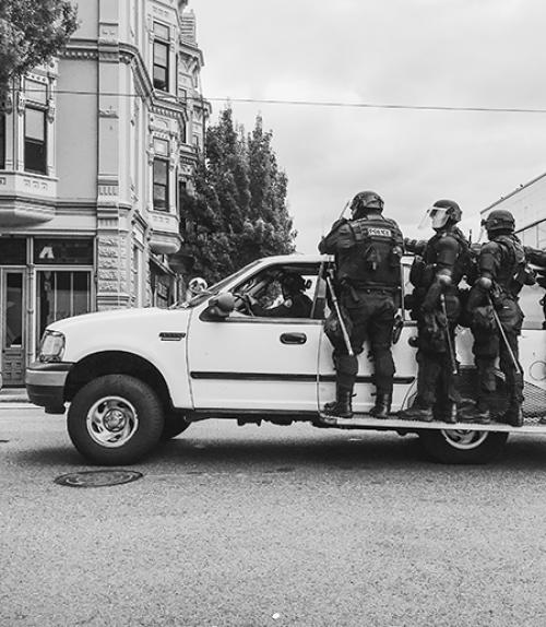 		 White truck carrying on side runners three police in riot gear 
	