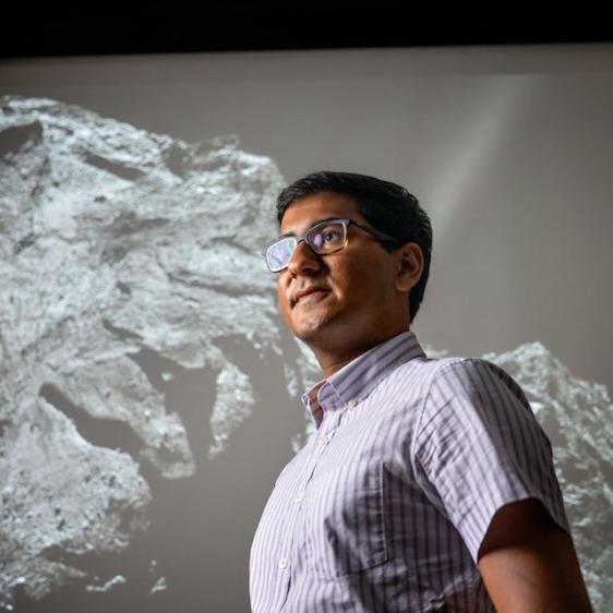 		Person standing in front of a huge black & white image of a comet with a rocky surface
	