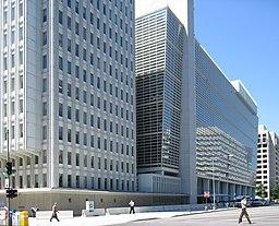 		Two multi-story gray buildings with people walking in front
	