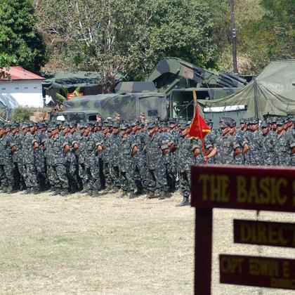 		Soldiers stand in formation beyond a wooden sign
	