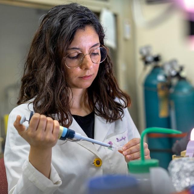 		Person in a white lab coat piping something into a test tube
	