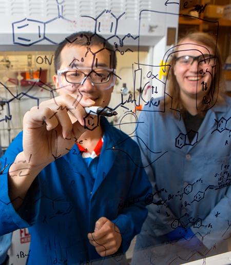 		 Two people write in marker on a clear wall
	