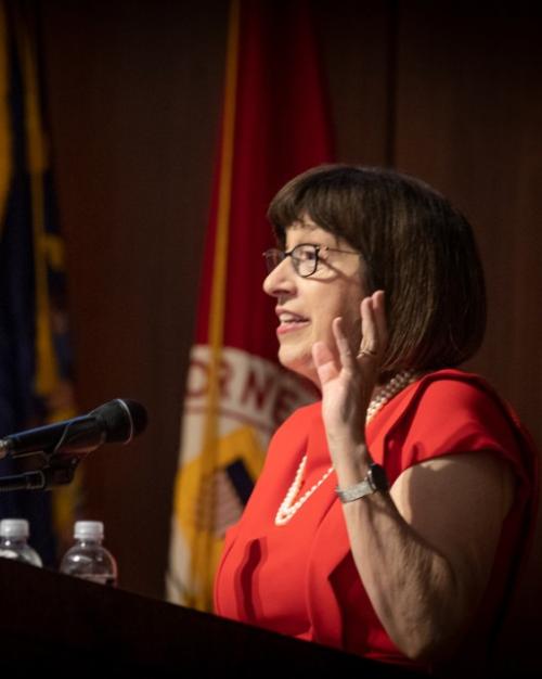 		Person wearing red and pearls, speaking at a podium
	