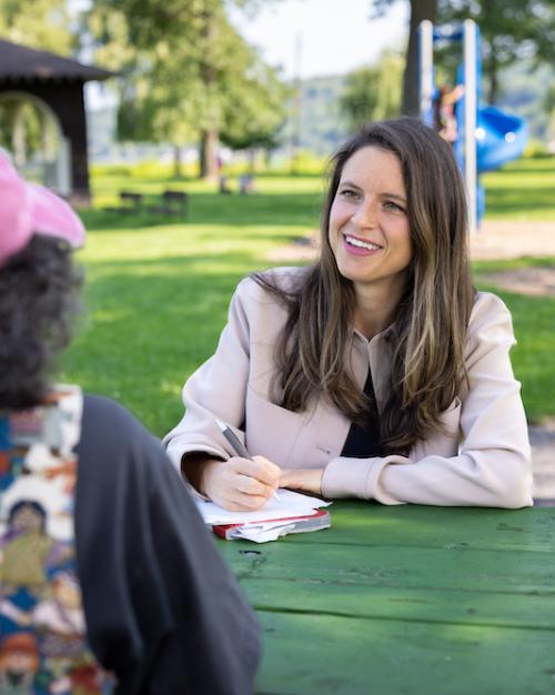 		Two people sitting at a table, conversing in a shady area of a park
	