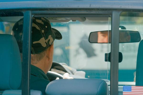 Person in the driver's seat of a pickup truck, seen through the back window