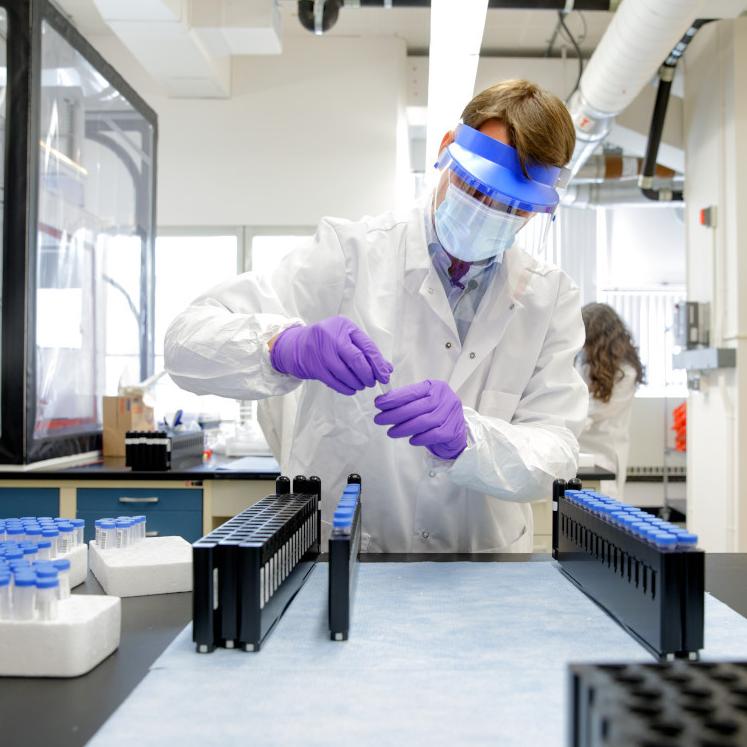 Person wearing protective lab gear handles virus test samples