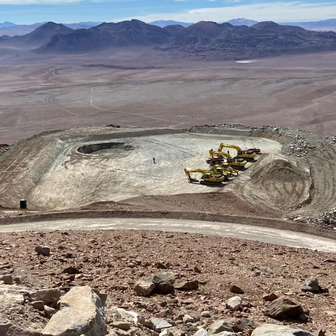 Flat ground and four construction vehicles; mountians in background