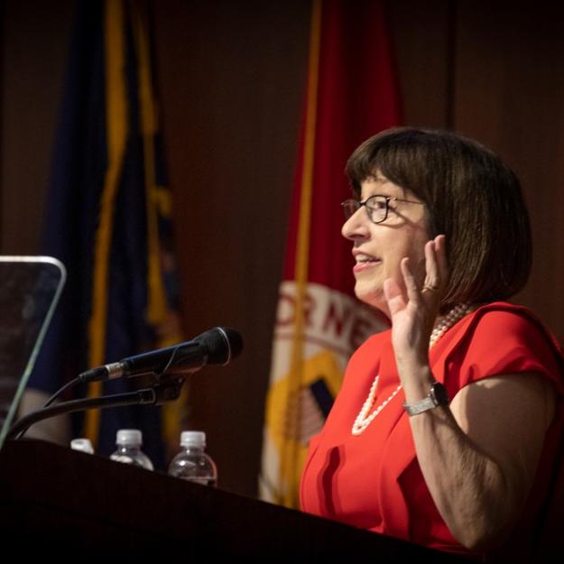 Person wearing red and pearls, speaking at a podium