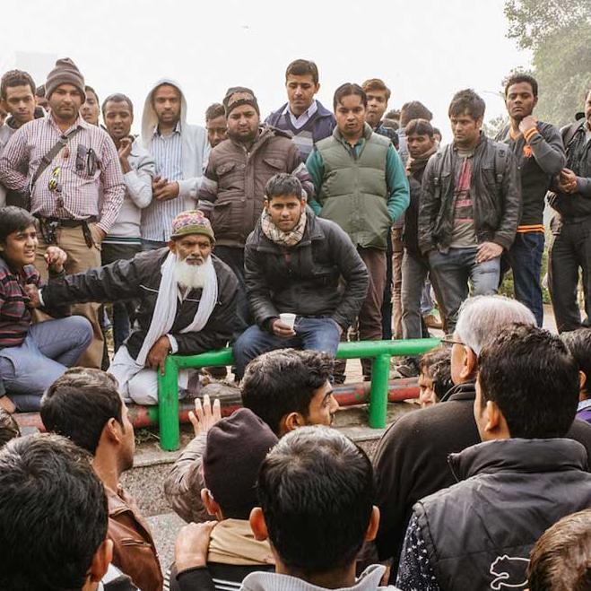 A few dozen men sit and stand in a group, talking intensely