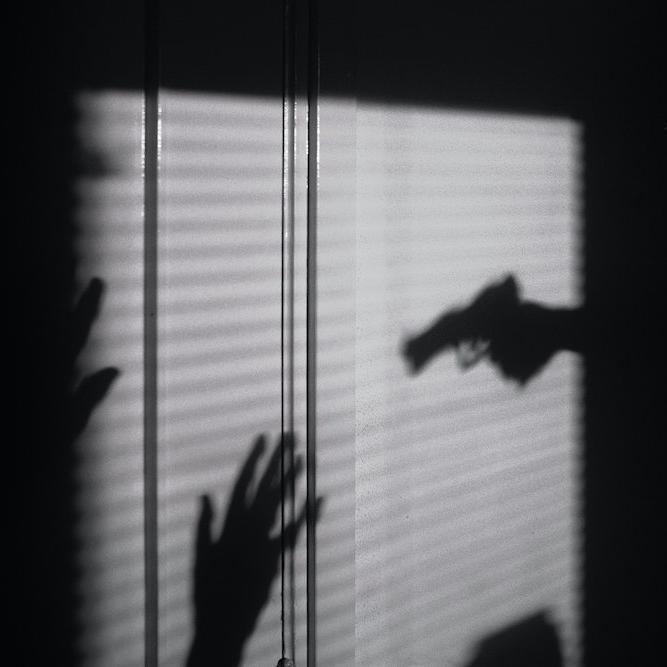 Silhouettes on a wall show a gun aimed at two hands held up in surrender; a scene of nighttime crime