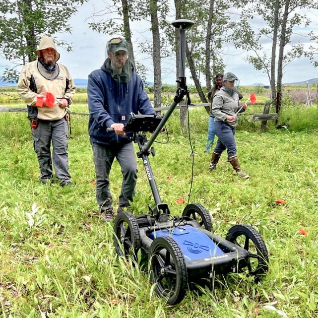 three people use a wheeled machine on a grassy plot of land