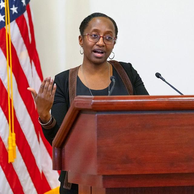 Person speaking at a podium; American flag in the background