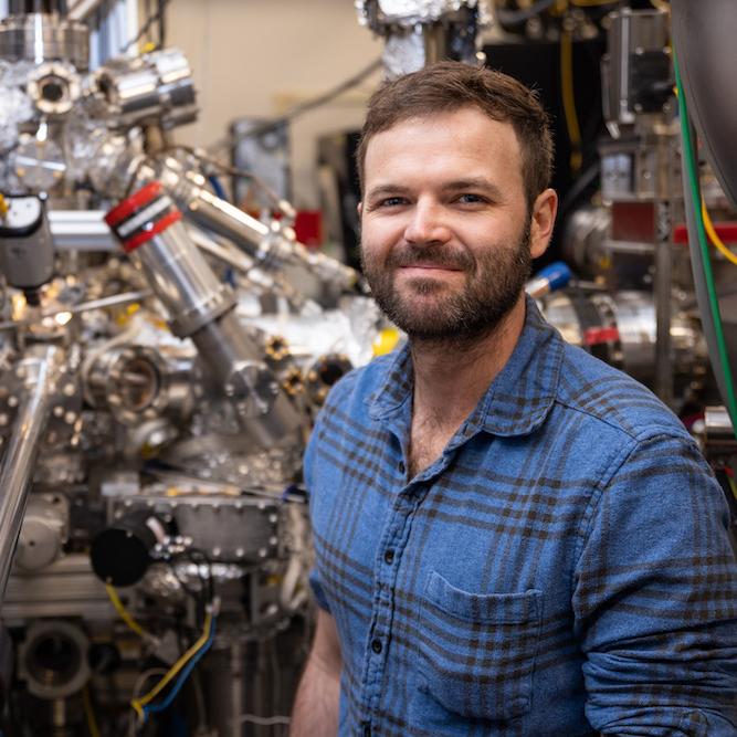 person wearing blue shirt stands in front of complicated silver equipment