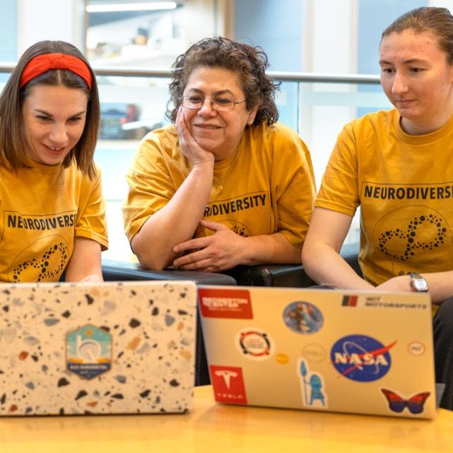 Three people wearing matching yellow t-shirts look at two laptop computers