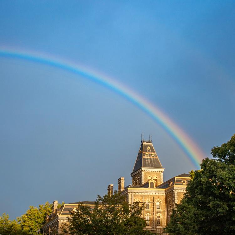 A rainbow against a deep blue sky, over a brick building with a peaked roof