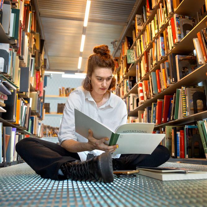 Person sitting on a floor surrounded by books on shelves