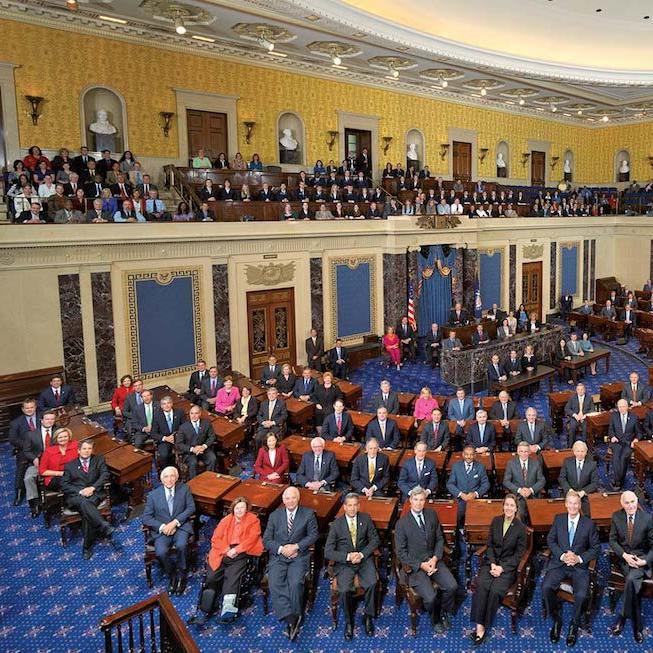 		The U.S. Senate chamber (blue carpet, yellow walls) with the Senators seated at their deks
	