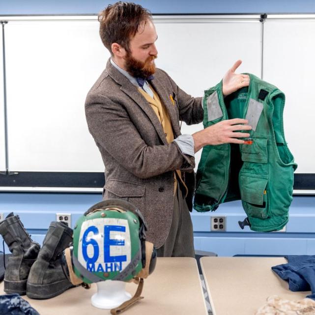 A person holds up a green vest -- a military flack jacket from the U.S. Navy