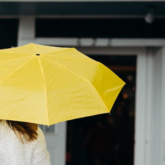 		Bright yellow umbrella held by a person wearing a white sweater. It's not raining. 
	