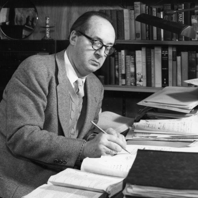 Historic black and white image: a person sitting at a desk, writing