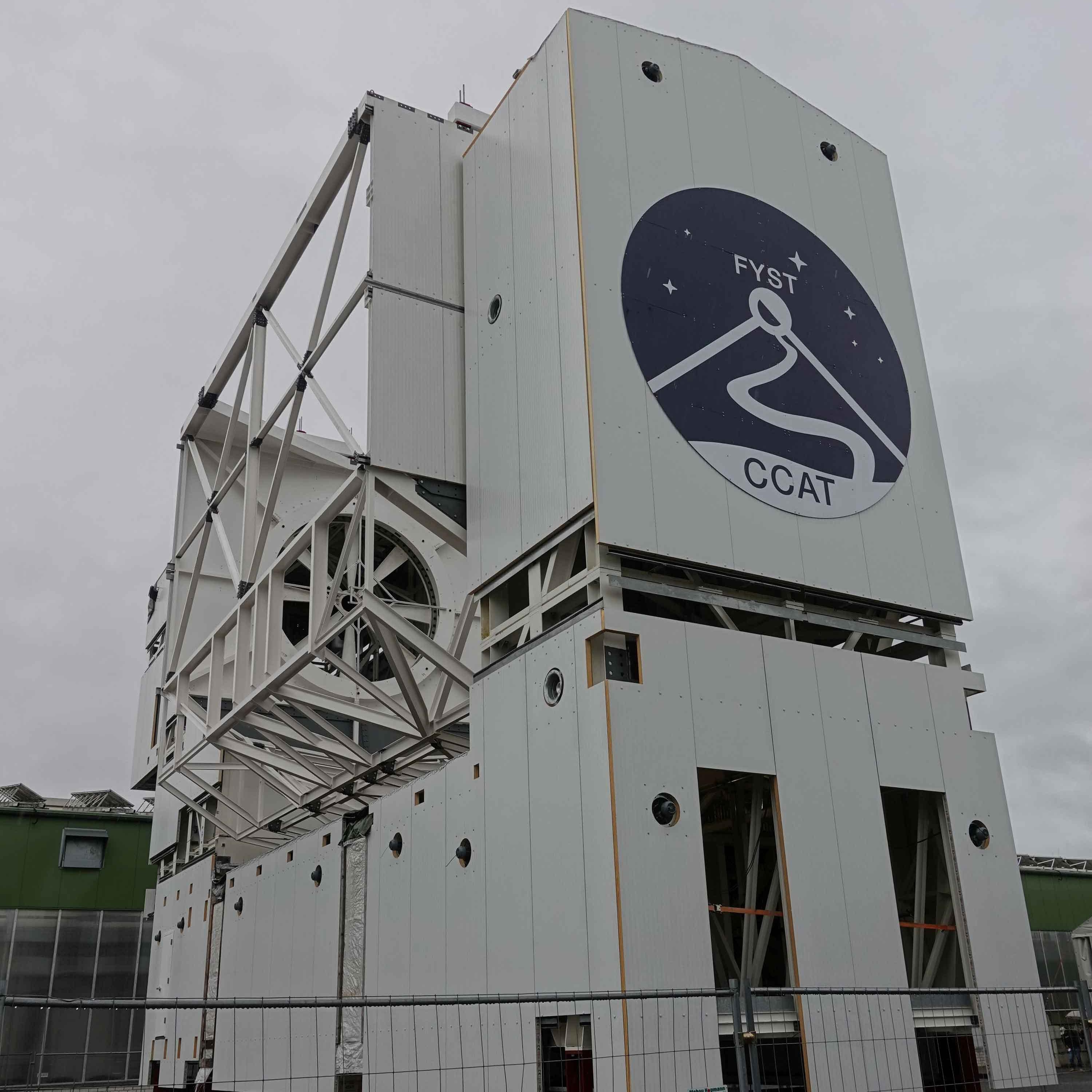 		The side of the telescope, showing the logo with "FYST" and "CCAT" and a line drawing of a road leading up a mountain
	