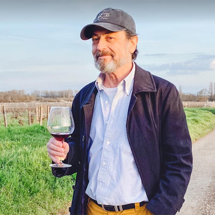 Person standing on th edge of a vineyard, hodling a glass with a little red wine in it