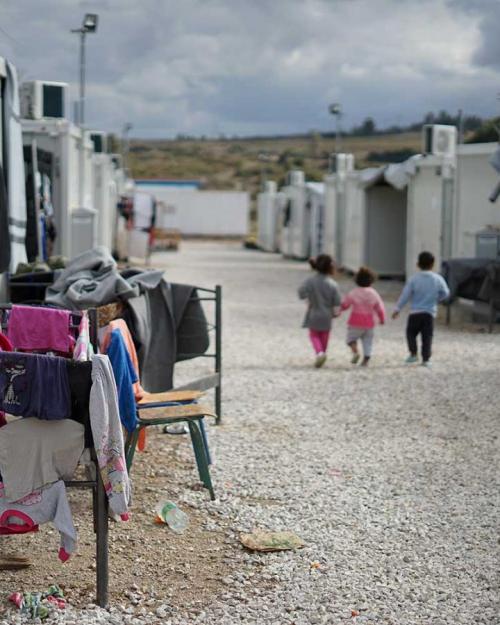 Three children walk away down a path between tents