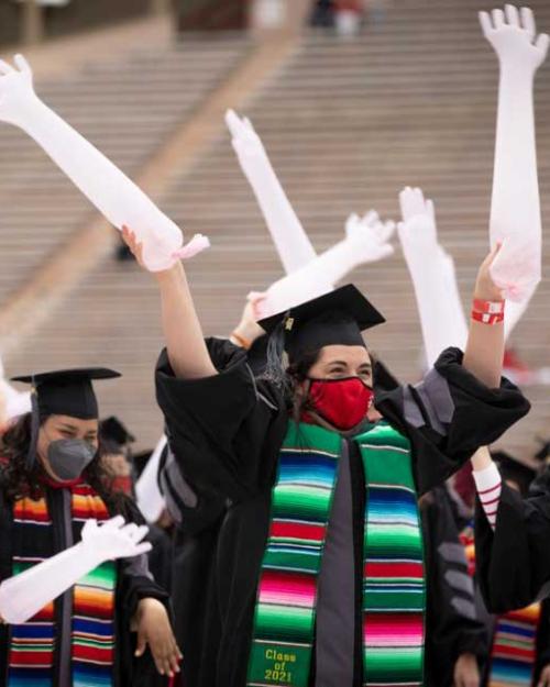 People in graduation caps and gowns wave balloons