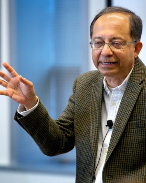 Kaushik Basu wearing a tweed jacket with hand upraised as he delivers a talk.