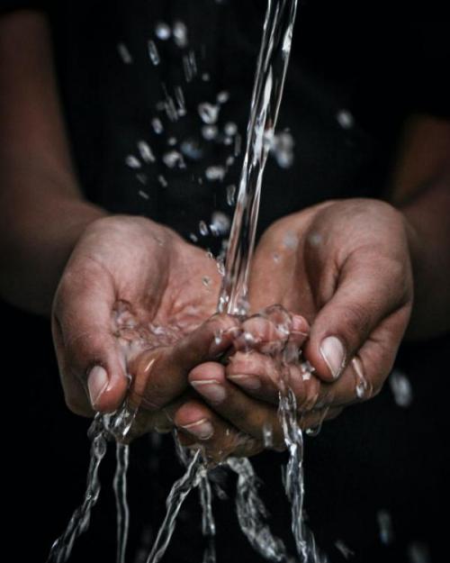 Dark-skinned person cupping hands under a stream of water. 