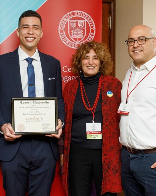 Conor Hodges in suit and tie, smiling and holding his award plaque, flanked by other alumni.