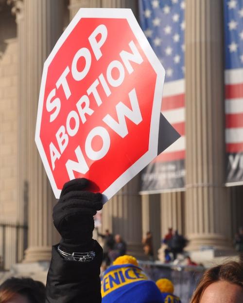 Red protest sign held up outside a stone-columned building