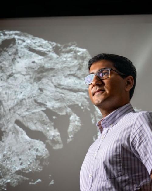 Person standing in front of a huge black & white image of a comet with a rocky surface