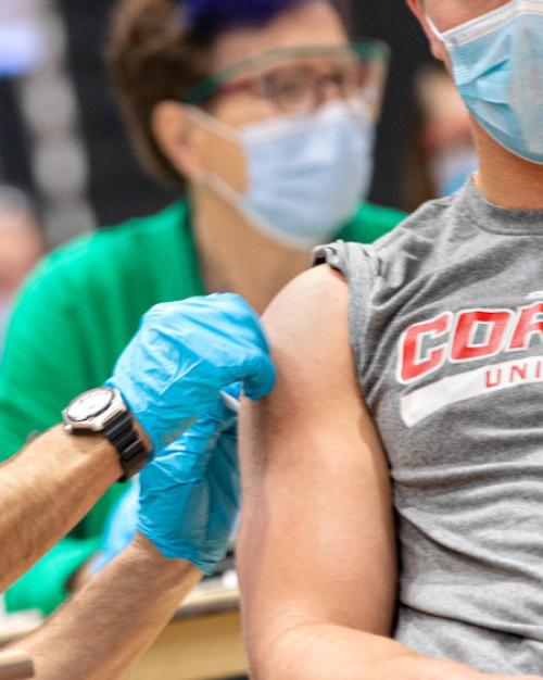 Medical professoional wearing a mask and protective gloves gives a shot to a person wearing a Cornell Big Red t-shirt