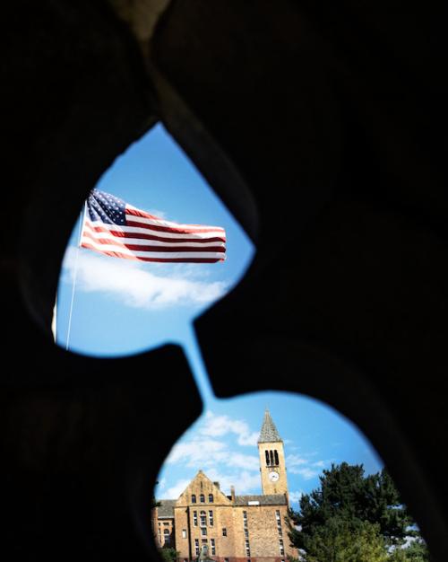 American flag, blue sky and campus building seen through a cutout shaped like an hourglass