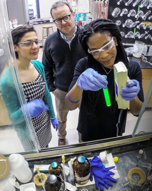 Three people handle chemistry equipment in a lab