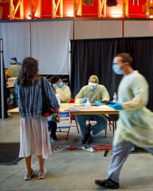 Person waits for a COVID test while people wearing medical gear hurry by