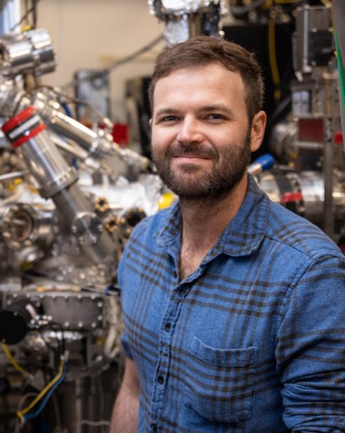 person wearing blue shirt stands in front of complicated silver equipment