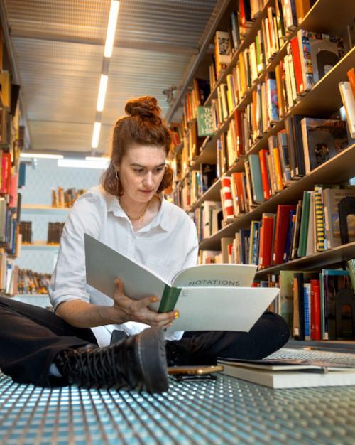 Person sitting on a floor surrounded by books on shelves