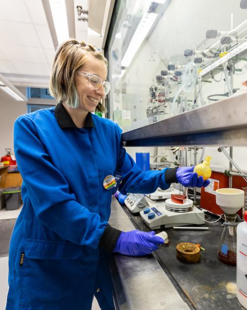 		Person in blue lab coat, standing at a counter full of instruments and bottles
	