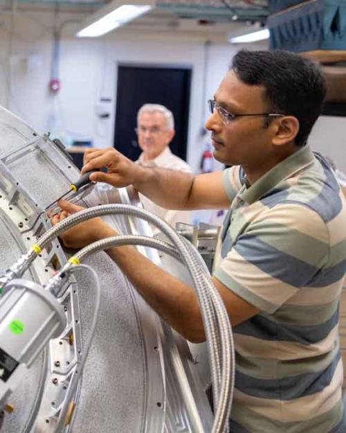 Amit Vishwas uses a screwdriver to work on ALPACA, a round metal top with metal boxes and cables protruding