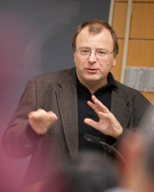 Nicolas van de Walle speaking, hands moving, wearing glasses and a jacket