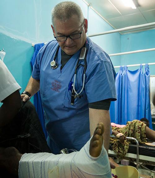  Doctor leaning over man with broken leg in hospital bed