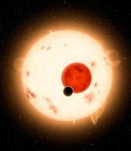  A large sun shines behind a red planet and a smaller black planet in space