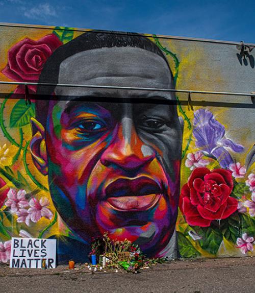  Artist drawing of George Floyd&#039;s face on a wall, surrounded by flowers and Black Lives Matter sign