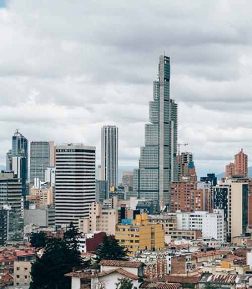  Tall silver buildings rise out of a sprawling city with mountains in the background