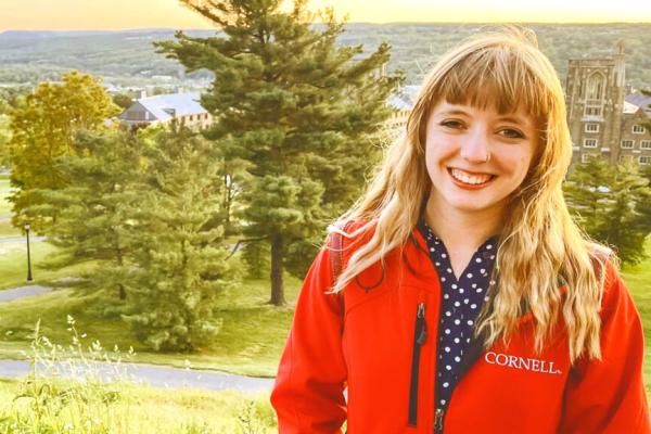 Lorlei Boyd, long blond hair and in a Cornell jacket, smiling with Libe Slope trees behind her