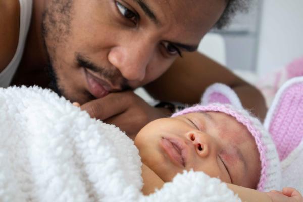 Man with mustache leaning close to sleeping baby wearing pink knitted ears